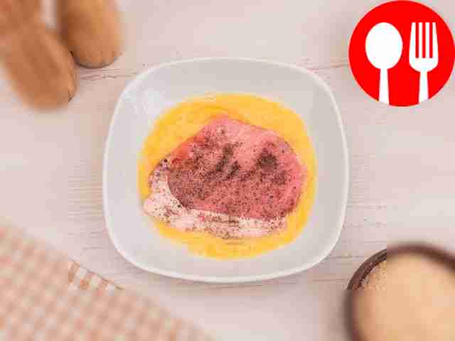 Окуните каждую свиную отбивную в яйцо.